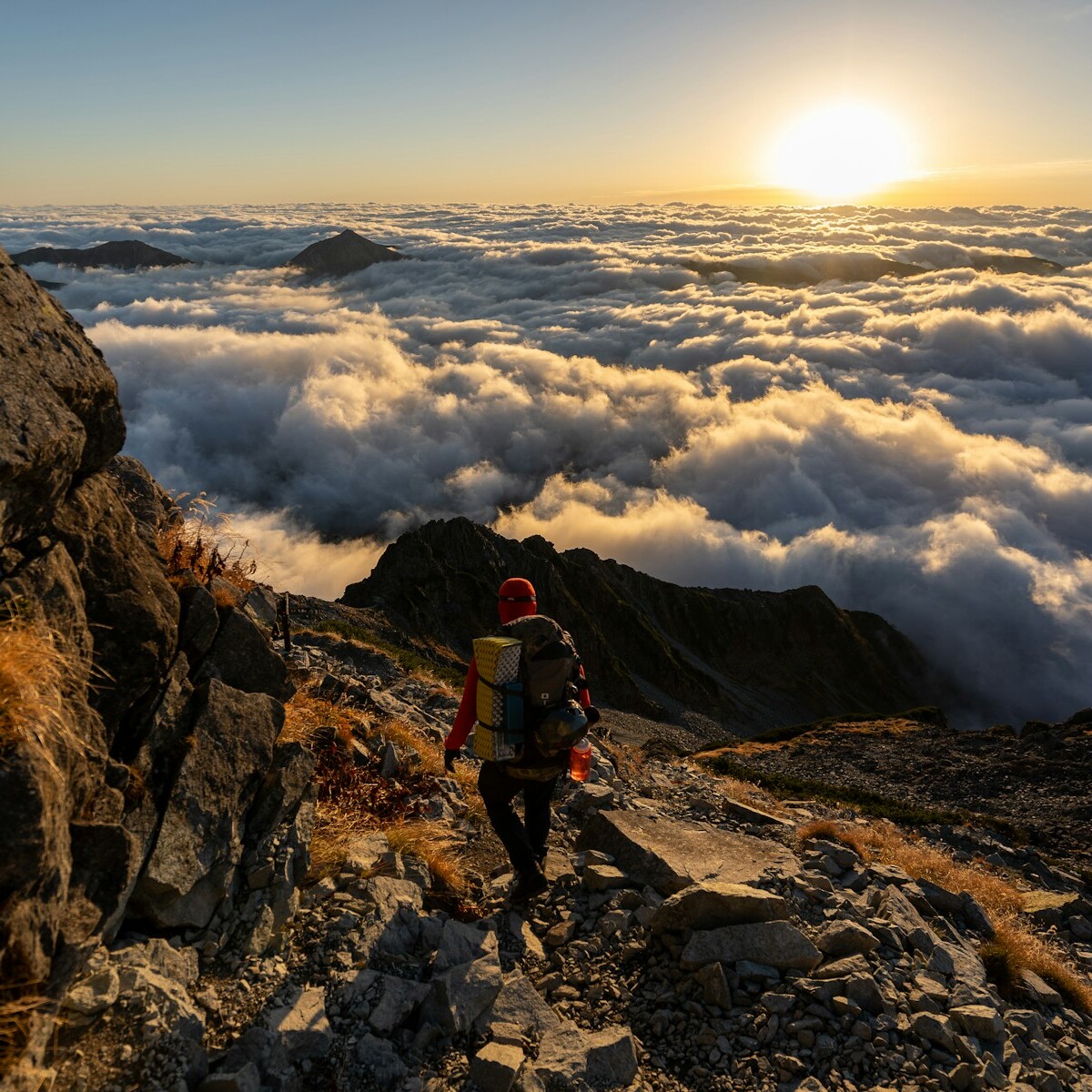 man in red jacket and black pants standing on rocky mountain during daytime