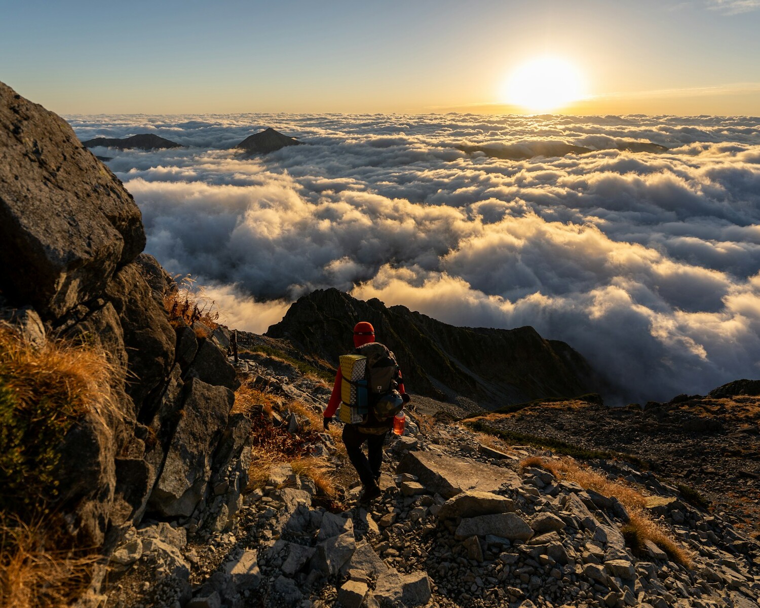 man in red jacket and black pants standing on rocky mountain during daytime